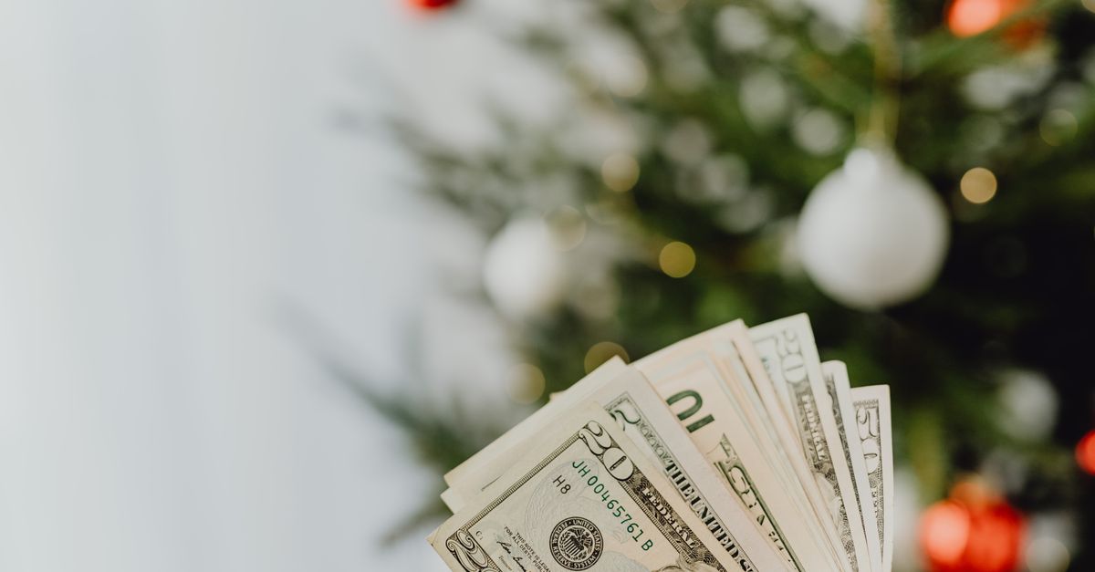 Stack of US dollar bills in front of a decorated Christmas tree, symbolizing holiday spending.